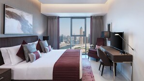 Ein modernes Hotelzimmer mit einem großen Bett, einem Schreibtisch, einem Fernseher und Blick auf eine Stadtsilhouette.