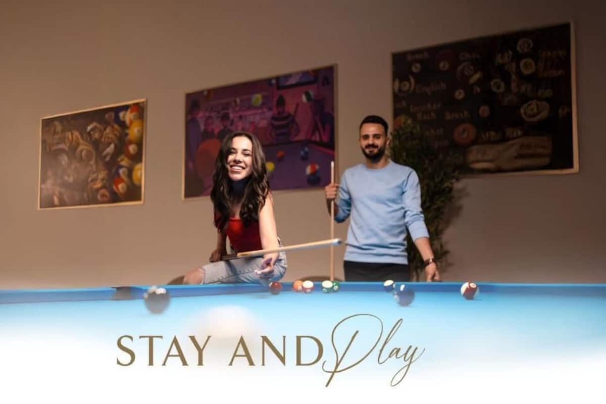 Ein Billardtisch mit dem Schriftzug "STAY AND Play" und zwei Personen beim Billardspielen.