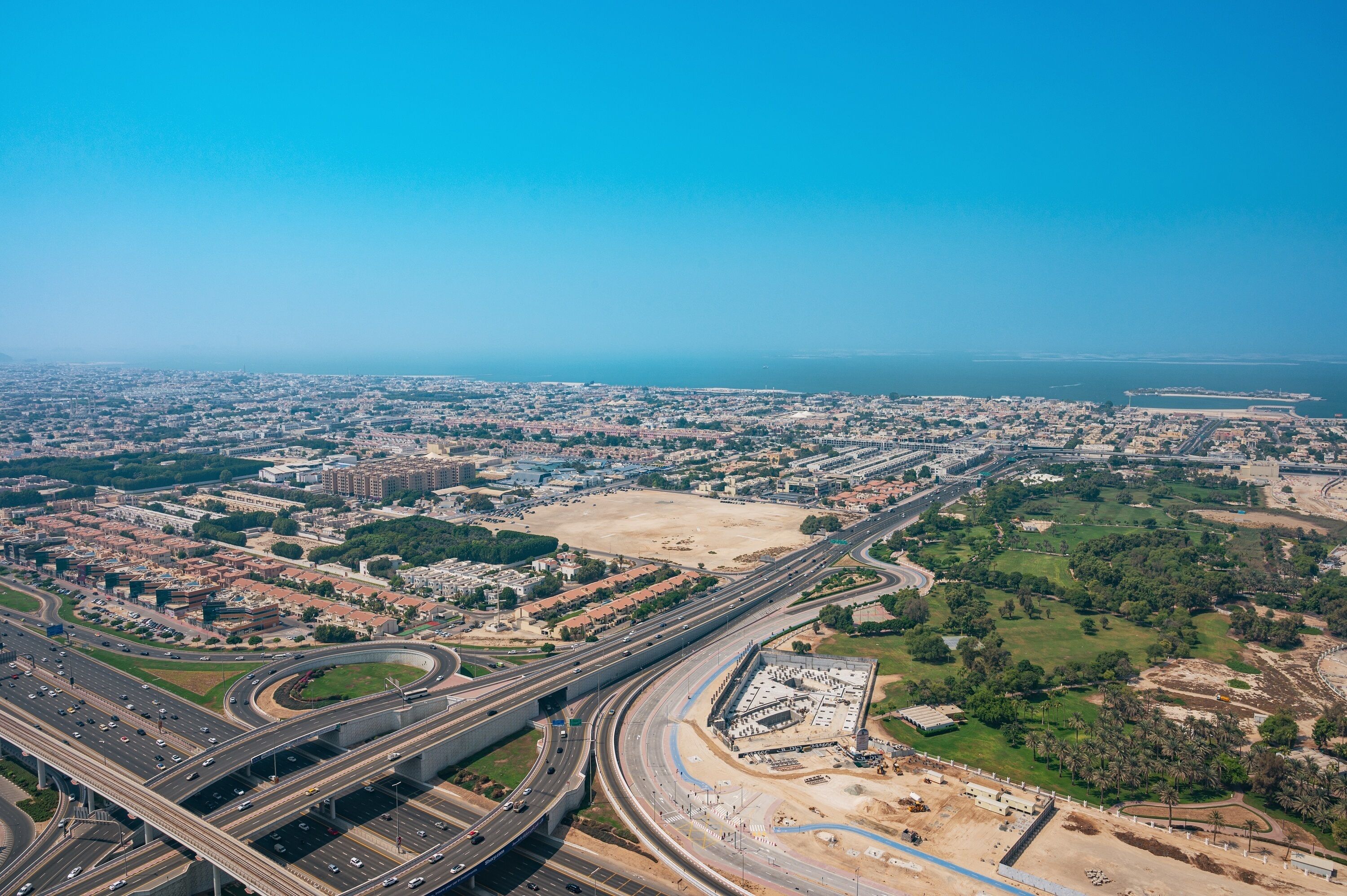 Vista aérea de un paisaje urbano con múltiples autopistas, una amplia zona abierta y zonas verdes circundantes.
