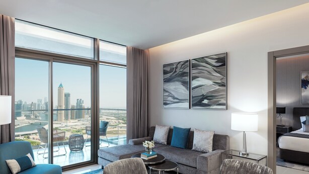 Ein modernes Hotelzimmer mit großem Fenster und Blick auf die Stadt, einer Couch, einem Esstisch und einem Bett.