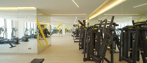 A modern gym with cardio machines, weight stations, and mirrors on the walls.