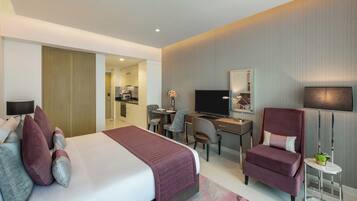 A modern hotel room with a large bed, a desk, a chair, a TV, and a small table with a plant.