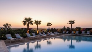 Ein Poolbereich mit Liegestühlen und Palmen vor einem Sonnenuntergangshimmel.