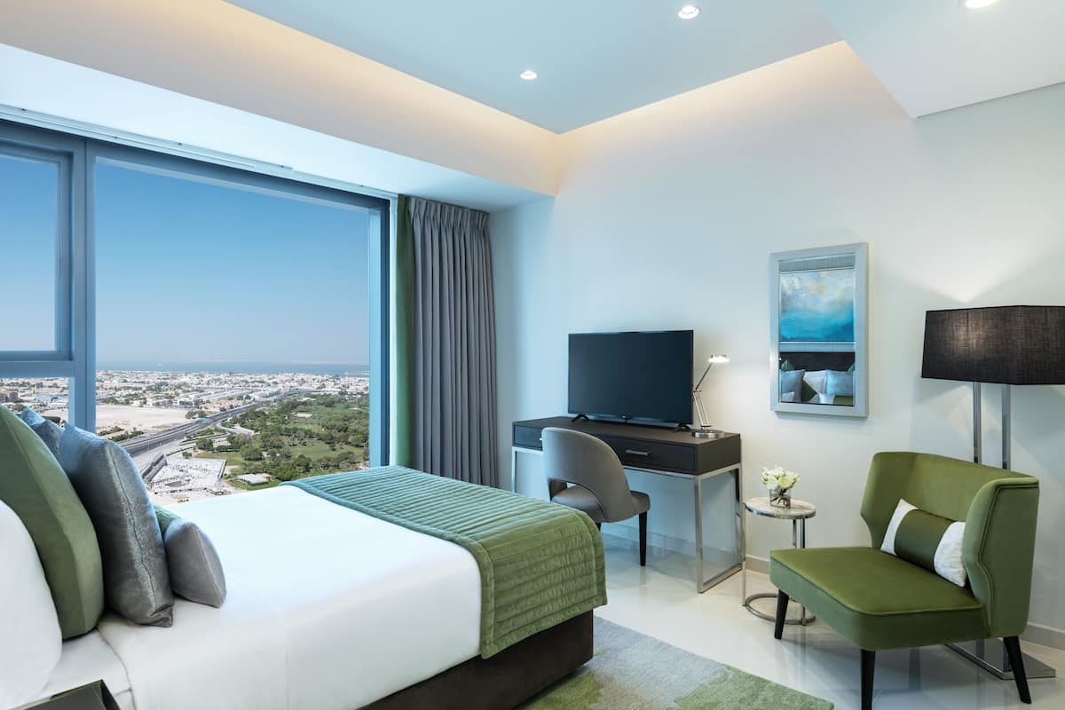 Ein modernes Hotelzimmer mit einem großen Bett, einem Schreibtisch, einem Stuhl, einem Fernseher und Blick auf die Stadt.