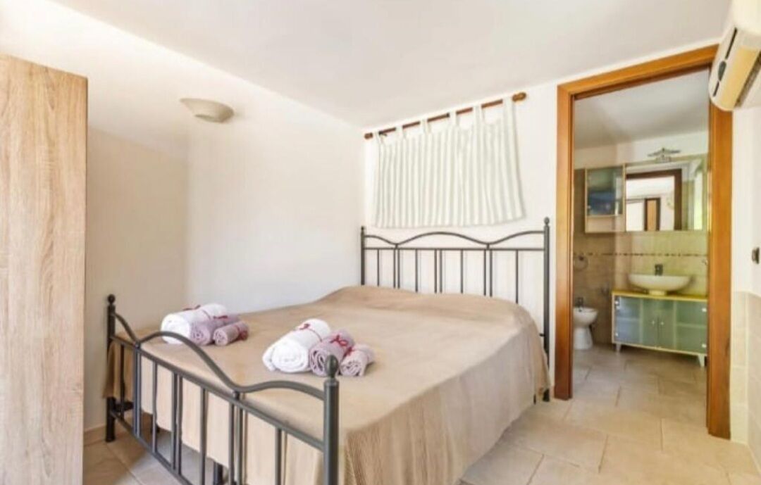 Un dormitorio con cama, un baño con lavamanos y espejo, y una puerta que da a otra habitación.
