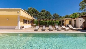 A pool area with clear water, a pergola with lounge chairs, and a yellow building. - Villa Dosagiri Stanza Privata+piscina (Selva di Fasano)
