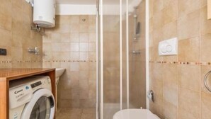 A bathroom with a glass-enclosed shower, a toilet, and a washing machine in a wooden cabinet. - Villa Dosagiri Stanza Privata+piscina (Selva di Fasano)