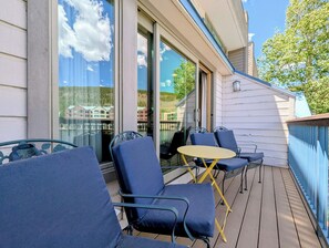 A balcony with blue chairs and a small table, a glass door, and a view of buildings and trees. - Keystone Lakeside Getaway | Summer Fun (Keystone)