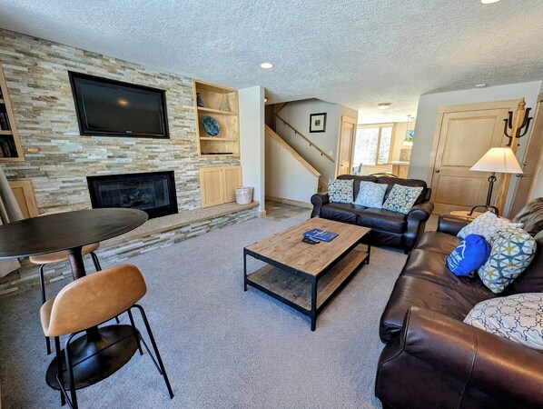 A living room with a stone fireplace, a flat-screen TV, a leather sofa, and a coffee table. - Keystone Lakeside Getaway | Summer Fun (Keystone)