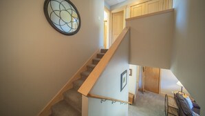 A staircase with a wooden handrail, carpeted steps, and a wall-mounted circular window.