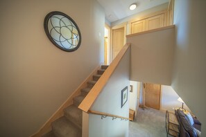 A staircase with a wooden handrail, carpeted steps, and a wall-mounted circular window.