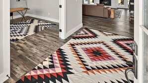 A spacious hallway with a patterned rug, a desk with a lamp, and a modern kitchen in the background. - New! Luxury Texas Farmhouse (Waco)