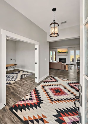 A spacious hallway with a patterned rug, a desk with a lamp, and a modern kitchen in the background. - New! Luxury Texas Farmhouse (Waco)