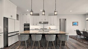 A modern kitchen with white cabinets, a granite island with bar stools, stainless steel appliances, and pendant lighting. - New! Luxury Texas Farmhouse (Waco)