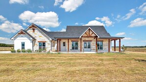 A large, single-story house with a stone facade, multiple windows, and a covered porch area. - New! Luxury Texas Farmhouse (Waco)
