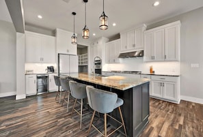 A modern kitchen with white cabinets, a central island with bar stools, and pendant lighting. - New! Luxury Texas Farmhouse (Waco)