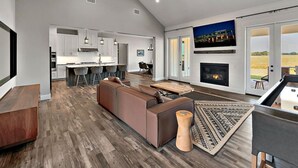 A spacious living area with a fireplace, a large TV, and a view of the outdoors. - New! Luxury Texas Farmhouse (Waco)