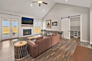 A spacious living room with a fireplace, a large window, and a ceiling fan. - New! Luxury Texas Farmhouse (Waco)