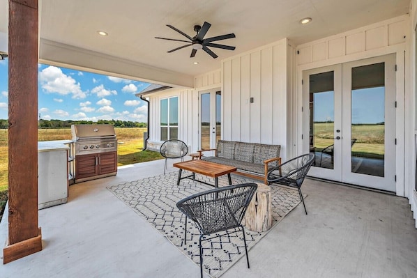 A covered patio with a grill, seating, and a ceiling fan. - New! Luxury Texas Farmhouse (Waco)