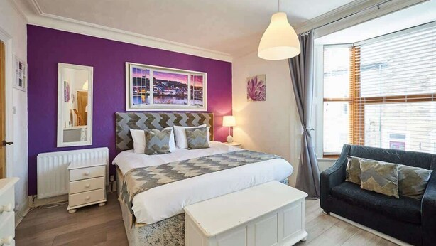 Une chambre à coucher avec un lit, une table de chevet, une lampe et une fenêtre avec des rideaux.