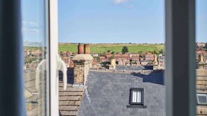 Une vue depuis une fenêtre donnant sur un quartier résidentiel, avec des maisons, un champ verdoyant et une cheminée.
