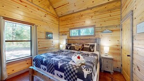 Un dormitorio de cabaña de madera con una cama, una mesita de noche, una ventana y una puerta.