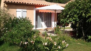 A house with a tiled roof, a covered patio with chairs, and a garden with flowering plants. - Studio Dans Propriété Avec Piscine au Calme Proche des Gorges du Verdon (Régusse)