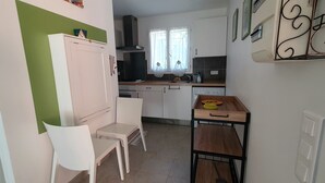 A compact kitchen with white cabinets, a wooden countertop, and a small dining area with a table and chairs. - Studio Dans Propriété Avec Piscine au Calme Proche des Gorges du Verdon (Régusse)