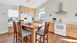 A modern kitchen with wooden cabinets, a white stove, and a dining area with wooden chairs.
