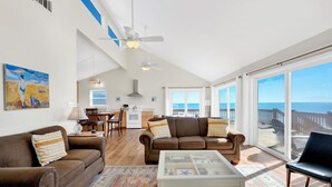 A spacious living area with two brown sofas, a coffee table, and a large window offering a view of the ocean.
