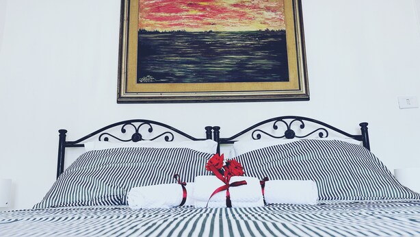 A bed with striped bedding, a framed painting above it, and a power outlet on the wall.