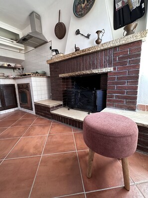 A kitchen with a brick fireplace, a wooden stool, and a tiled floor. - Vrbo Property (Subiaco)