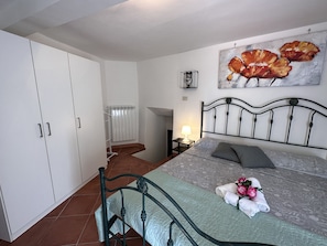 A bedroom with a bed, a radiator, a nightstand, and a painting on the wall. - Vrbo Property (Subiaco)