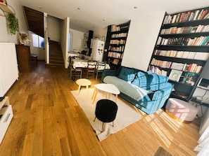 Una sala de estar con un sofá, una mesa de centro, una mesita auxiliar, una estantería y una escalera que lleva a otra habitación.