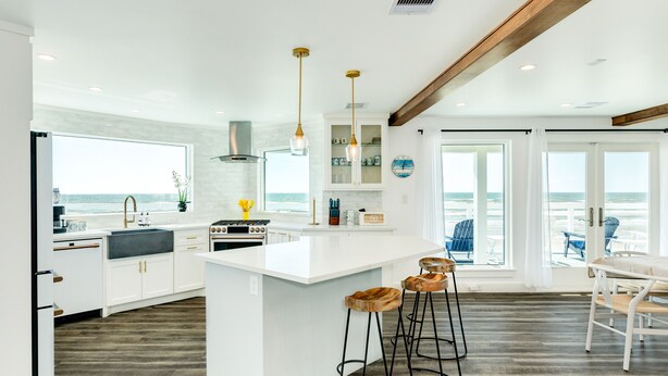 A modern kitchen with white cabinetry, a large island with stools, and a view of the ocean through large windows.