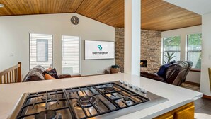 Una cocina moderna con estufa a gas central, pared de acento de piedra y un cartel de Bennington Properties.