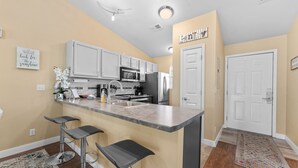A modern kitchen with white cabinets, a marble countertop, and a bar stool area.