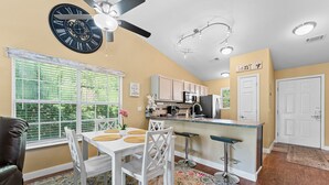 A kitchen with a bar area, a dining table with chairs, and a ceiling fan.