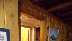 A wooden interior with a door leading to another room, a framed picture on the wall, and a patterned rug on the floor.