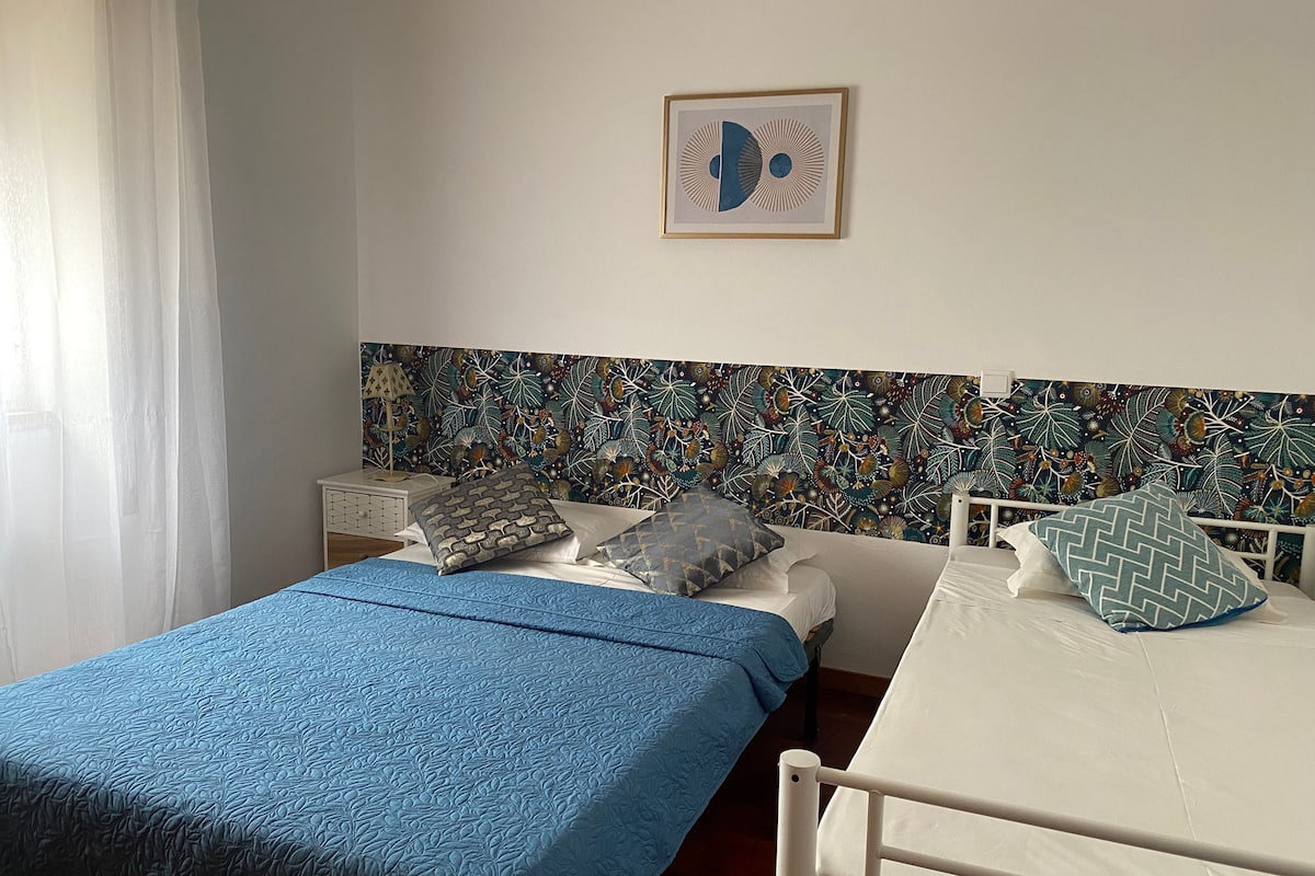 A bedroom with two beds, a patterned headboard, a nightstand, and a framed picture on the wall.