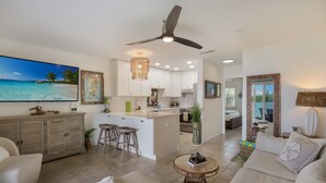 A spacious living area with a large flat-screen TV, a ceiling fan, and a kitchen with white cabinets and a central island. - Luxurious bungalow in Longboat Key (Longboat Key)