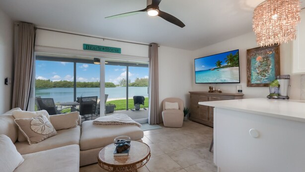 A modern living room with a sofa, a coffee table, and a TV. There's a sign that reads "Beach House" and a view of a lake through the glass doors. - Luxurious bungalow in Longboat Key (Longboat Key)