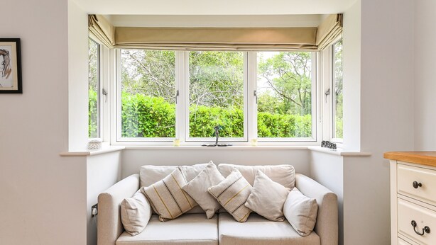 A room with a beige sofa, a window with a view of greenery, and a white dresser. - Woodland Cottage by inspirestays.com - a cottage that sleeps 2 guests in 1 bedroom (Duncton)