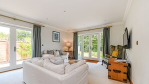 A spacious living room with a white sofa, a wooden chest, and a television on the wall. - Woodland Cottage by inspirestays.com - a cottage that sleeps 2 guests in 1 bedroom (Duncton)