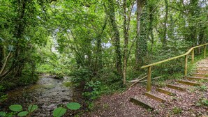 A wooden staircase leading up to a platform in a forested area with a stream. - Woodland Cottage by inspirestays.com - a cottage that sleeps 2 guests in 1 bedroom (Duncton)