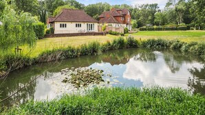 A house with a pond in front, surrounded by greenery and trees. - Woodland Cottage by inspirestays.com - a cottage that sleeps 2 guests in 1 bedroom (Duncton)