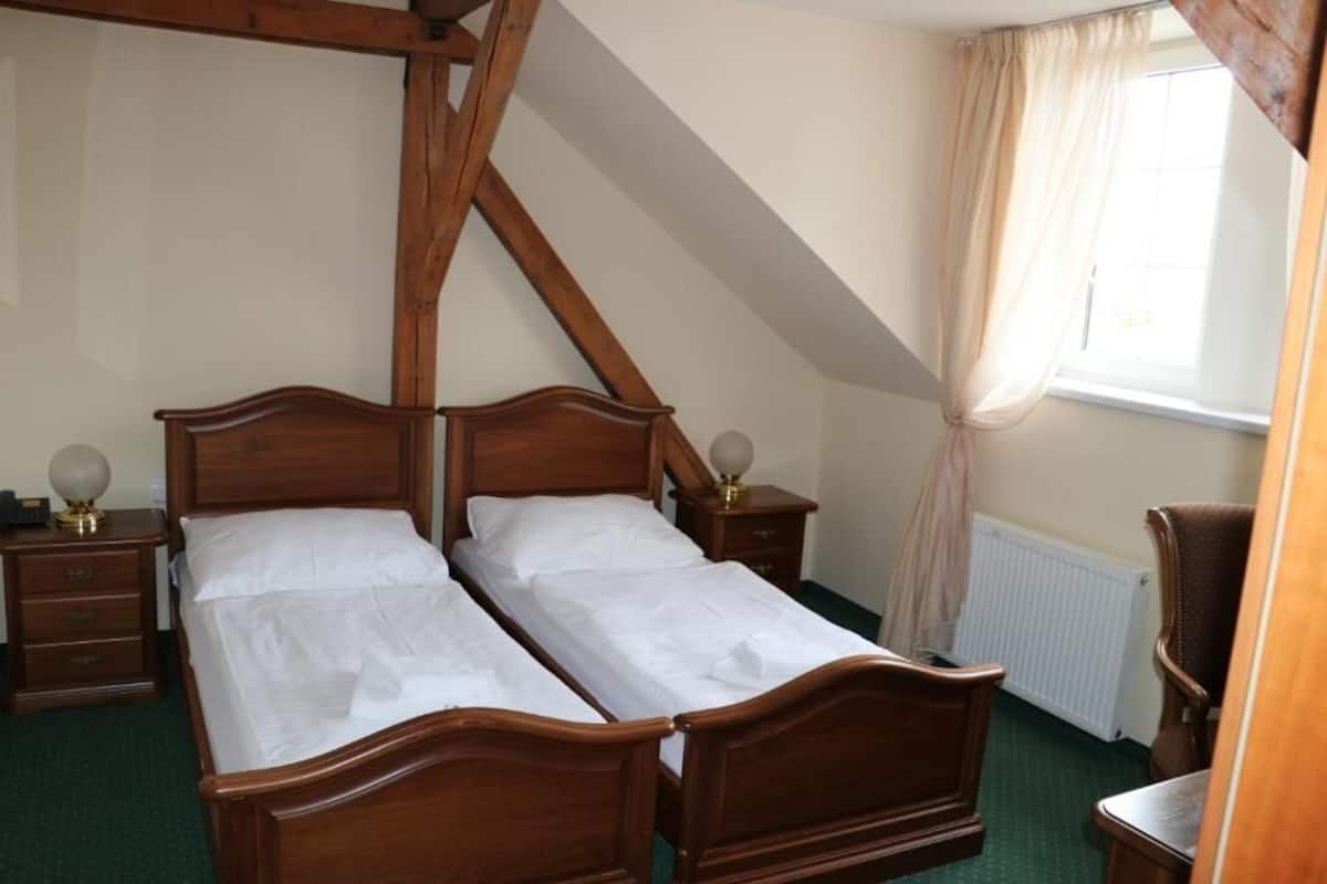 A room with two wooden beds, a nightstand with a lamp, a chair, and a window with curtains.