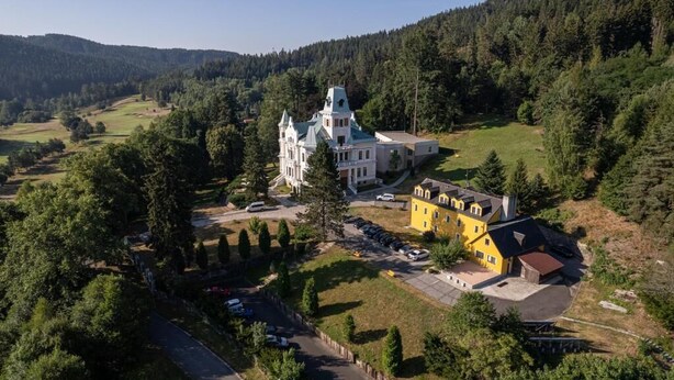 A large estate with a prominent white building featuring a tower, surrounded by lush greenery and a parking area. - Hotel U Zámečku Cihelny (Karlovy Vary)