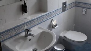 A bathroom with a white sink, a mirror, a toilet, and a trash bin. - Hotel U Zámečku Cihelny (Karlovy Vary)