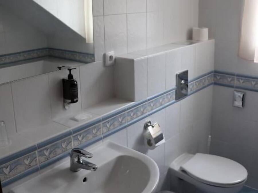 Een badkamer met een wit wastafel, een spiegel, een toilet en een vuilnisbak.